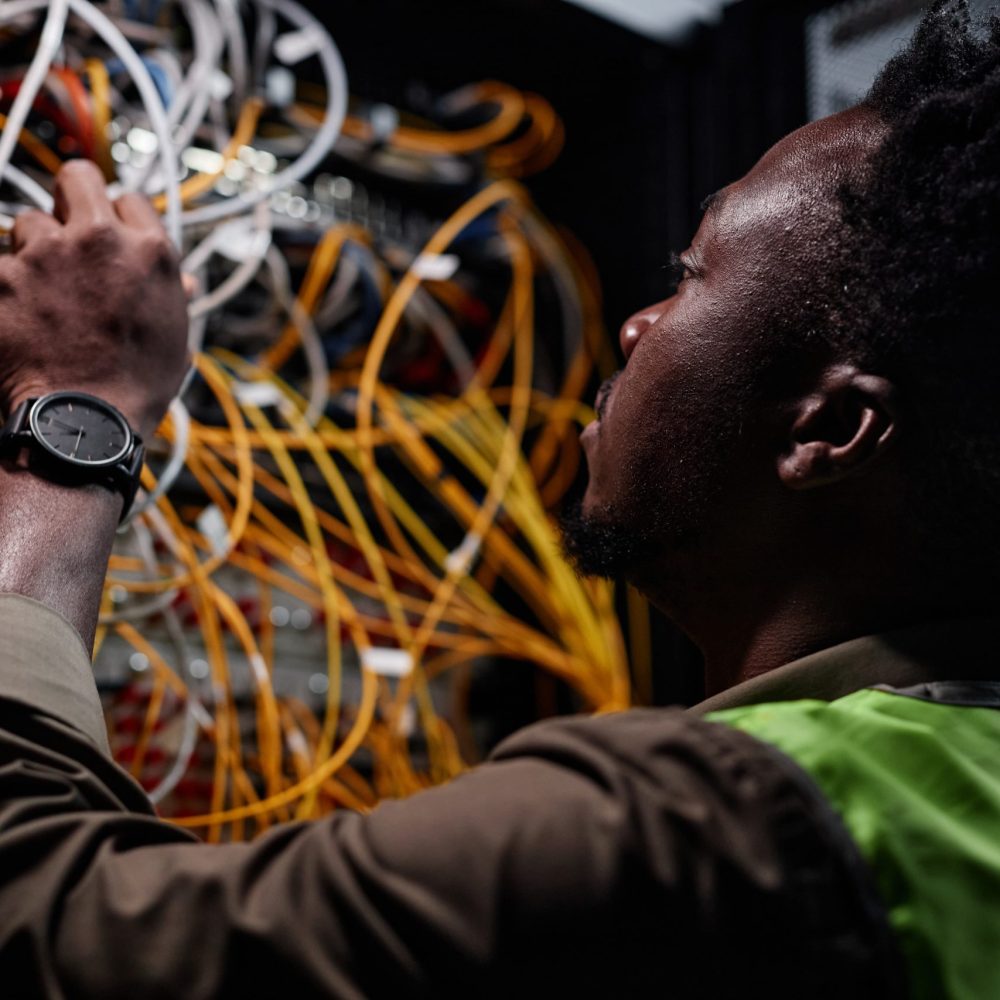 Close up of black man as network technician connecting cables and wires while repairing server in data center